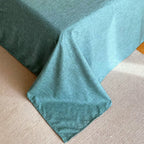 Coin d'une housse de couette en percale de coton vert canard retombant au pied du lit