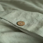 Gros plan sur un bouton en bois et la texture d'une housse de couette en lin vert amande