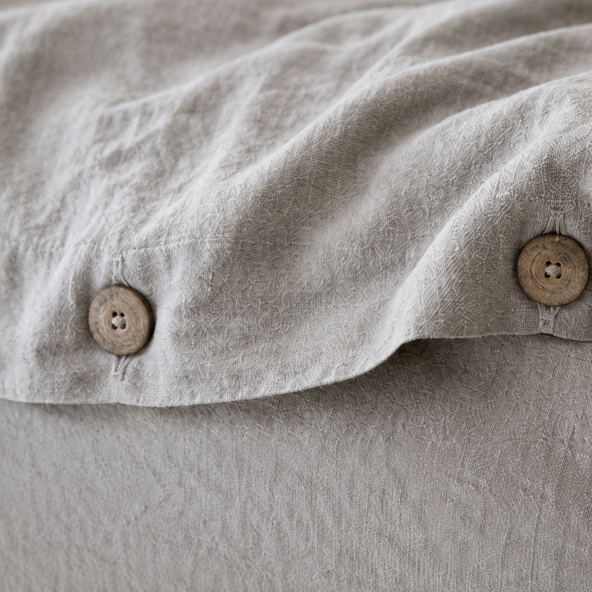 Gros plan sur les boutons en bois et la texture froissée d'une housse de couette en lin gris naturel