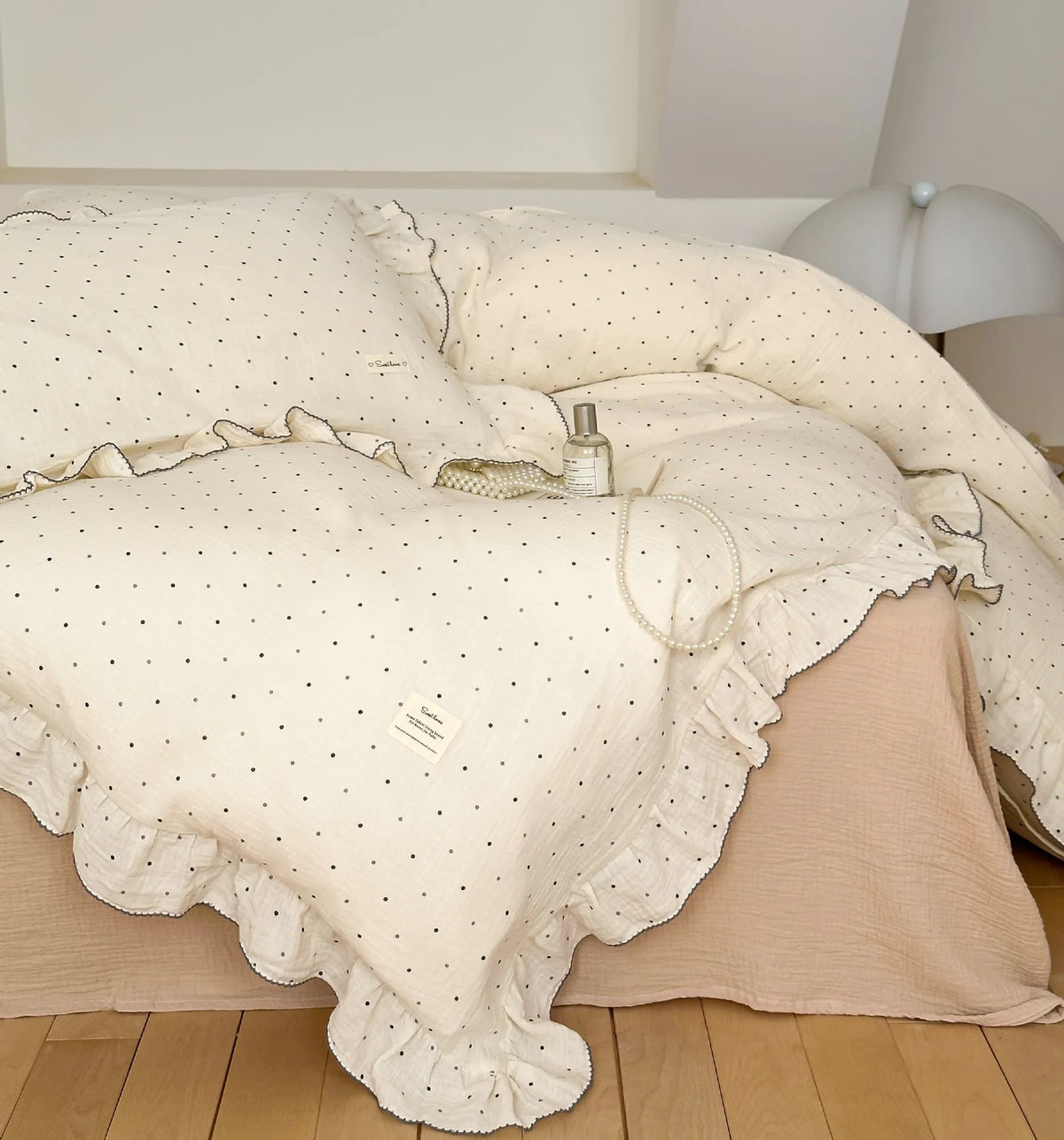 Housse de couette en gaze de coton écrue à petits pois noirs, bordée de volants, sur un lit