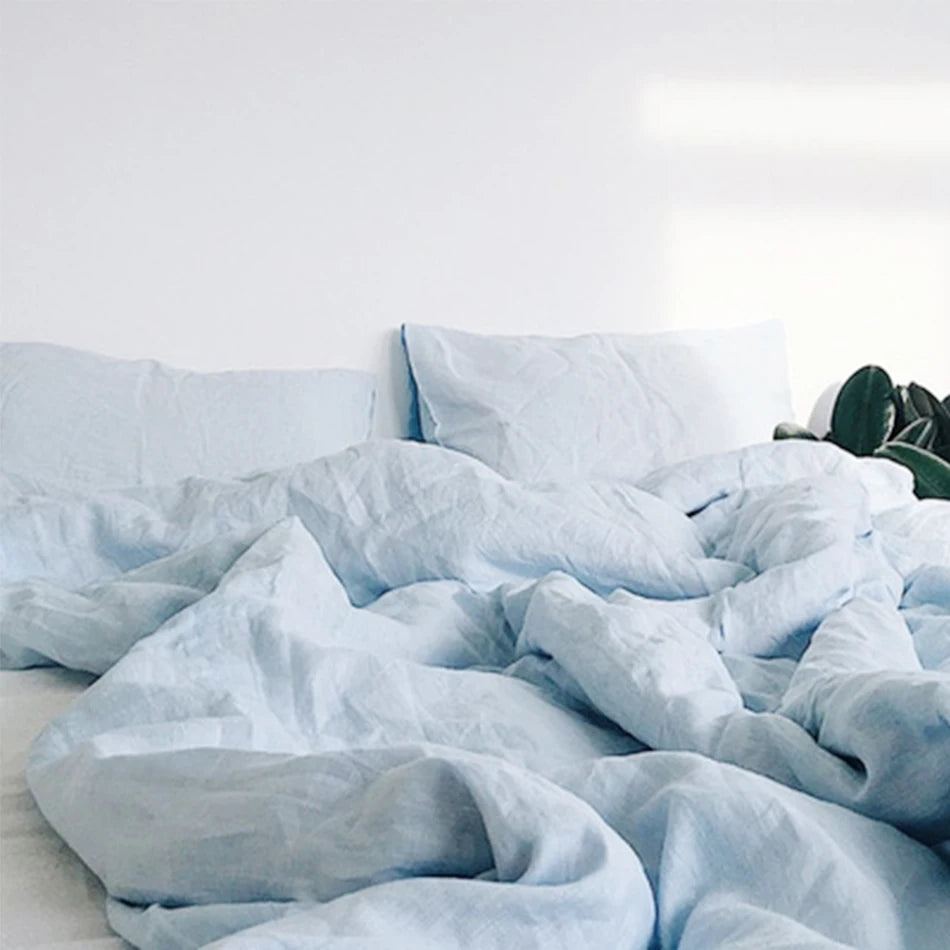 Housse de couette et taies d'oreiller en lin bleu clair froissé sur un lit défait
