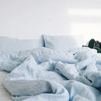 Housse de couette et taies d'oreiller en lin bleu clair froissé sur un lit défait