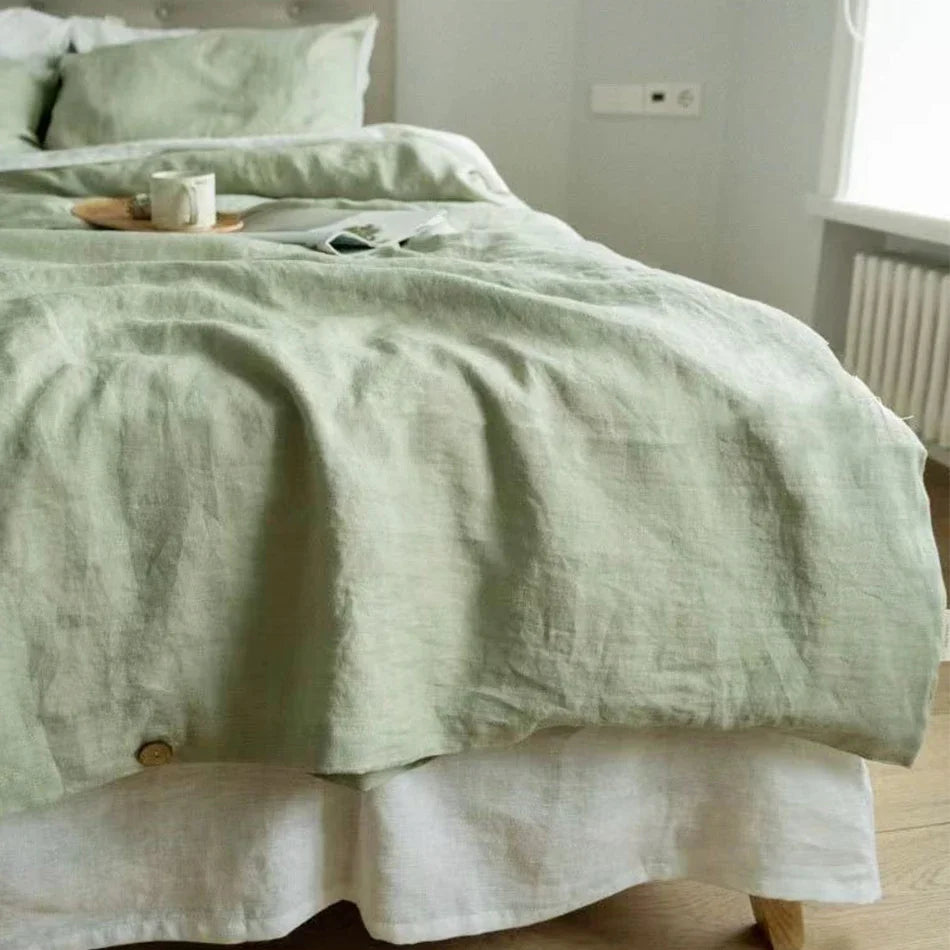 Housse de couette en lin vert amande froissée sur un lit, au-dessus d'un drap blanc