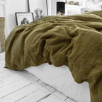 Housse de couette en lin vert kaki froissé tombant sur le côté d'un lit au drap blanc