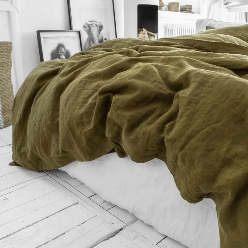 Housse de couette en lin vert kaki froissé tombant sur le côté d'un lit au drap blanc