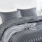 Housse de couette en satin gris anthracite à rayures sur un lit, vue de trois quarts avec taies