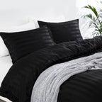 Vue rapprochée d'une housse de couette et de taies d'oreiller en satin noir à rayures ton sur ton