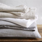 Pile de linge de lit en lin plié dans des tons beige, blanc et gris, à l'aspect froissé