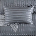 Taie d'oreiller en satin gris anthracite à rayures posée sur la housse de couette assortie