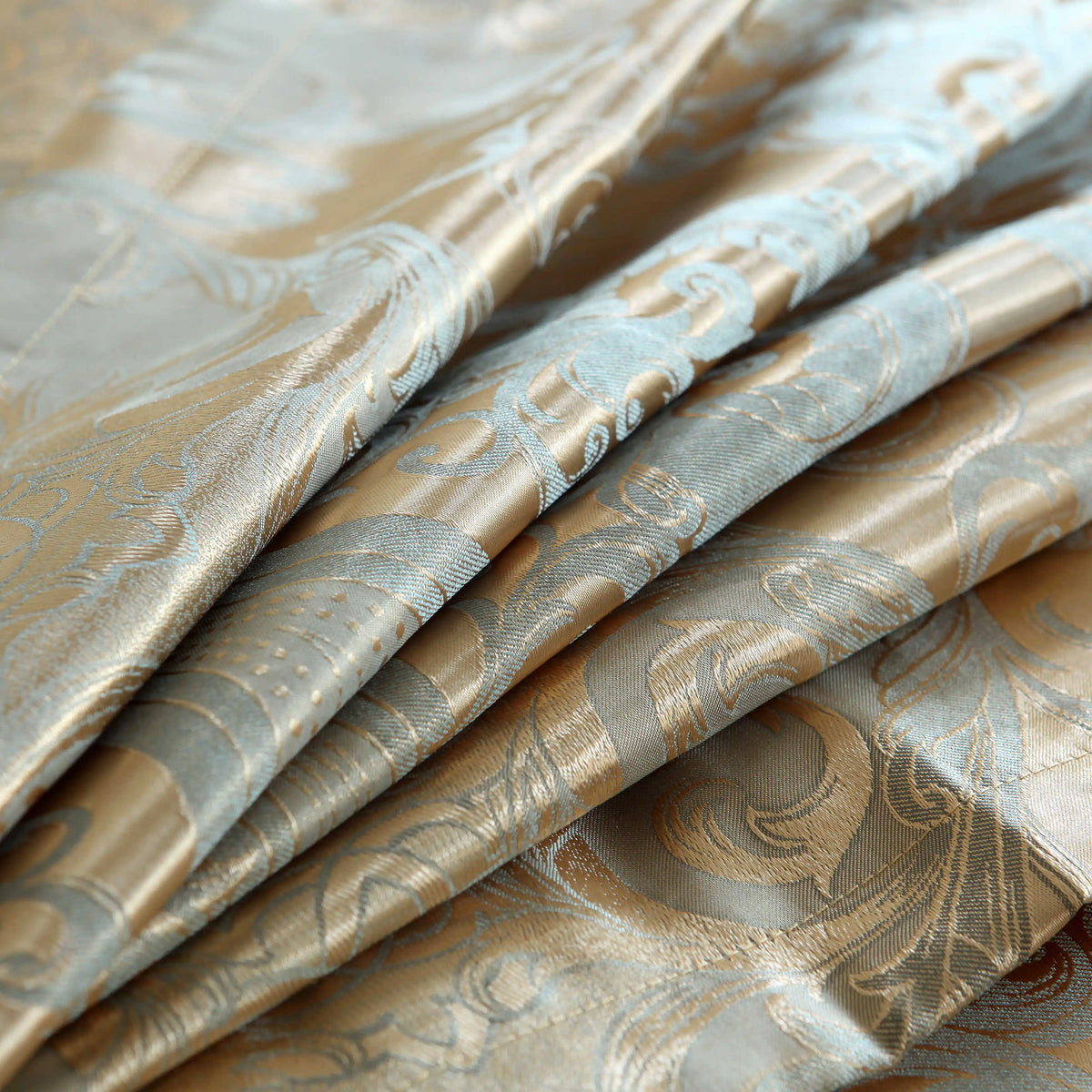 Gros plan sur les plis du tissu en satin damassé doré et gris bleuté d'une housse de couette